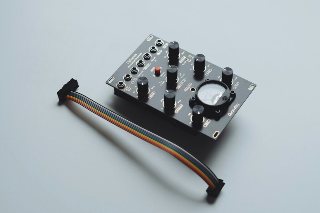 A black electronic module with knobs and a cable